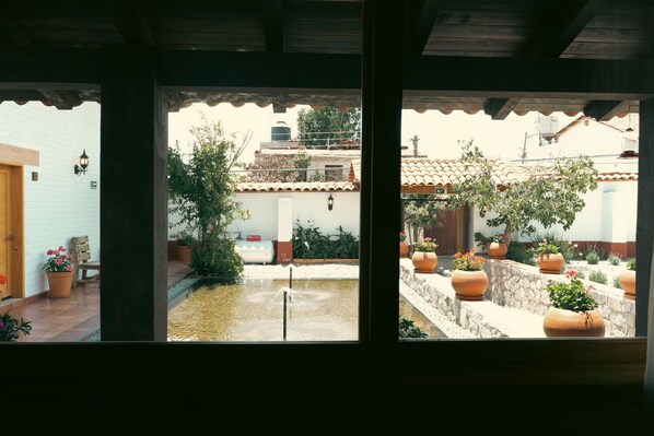 A courtyard with a water feature, potted plants, and a view of a building with a tiled roof. - Tapalpa Hotel Casa Colibrí (Tapalpa)