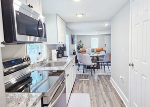 Eine moderne Küche mit Edelstahlgeräten, ein Essbereich mit rundem Tisch und Stühlen sowie ein Wohnzimmer mit Sofa und Couchtisch.
