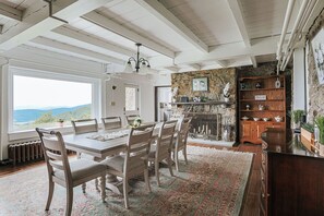 Un espace repas comprenant une grande table, des chaises, un lustre, un mur en pierre et un buffet en bois doté d’étagères.