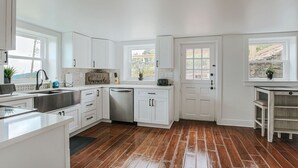 Una cocina con armarios blancos, un lavamanos de acero inoxidable y piso de madera.
