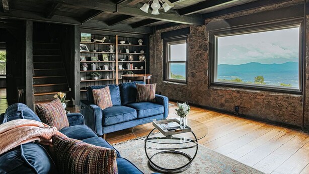Una sala de estar con un sofá azul, una estantería y un ventanal con vistas.