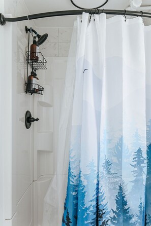 A shower curtain with a forest pattern, a wall-mounted soap dispenser, and a showerhead.