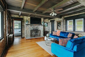 Un salon rustique avec une cheminée en pierre, un canapé bleu et un plafond en bois.