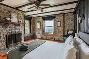 Une chambre avec un mur en pierre, un lit, une cheminée et une vue sur la mer.
