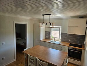 Una cocina compacta con una mesa de madera, armarios blancos, un horno empotrado y una ventana.