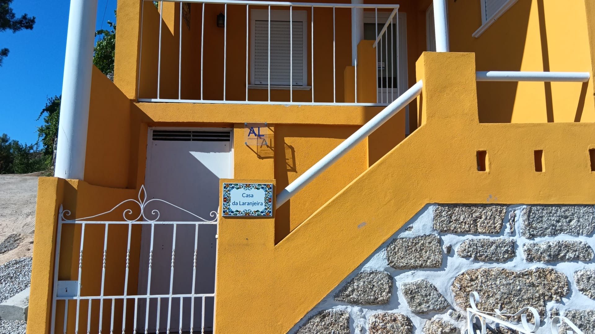 A yellow building with a stone wall entrance, a metal gate, and a sign reading 'Casa da Laranjeira.'