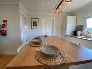 Comedor con una mesa de madera preparada para cuatro, un extintor y una cocina con vistas.