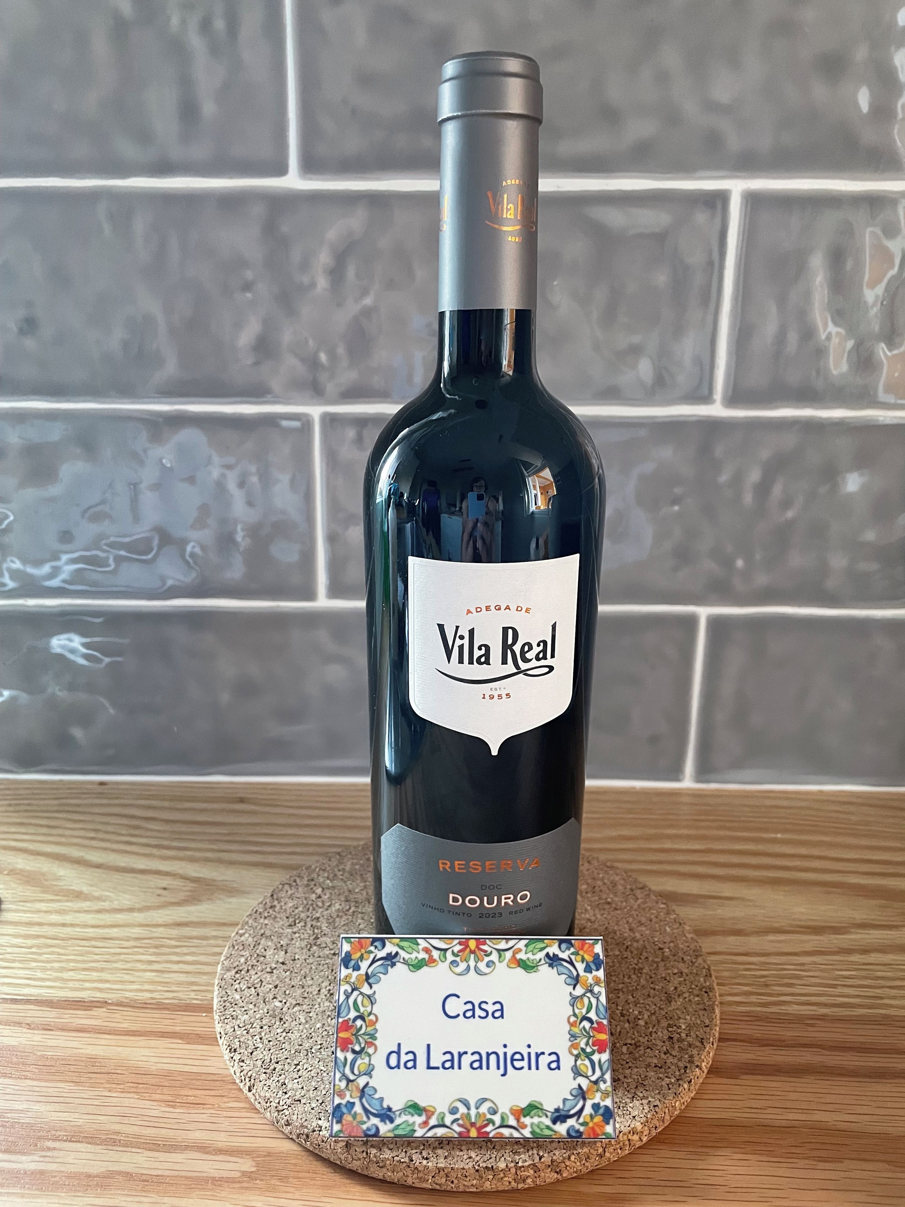 A bottle of Vila Real wine on a cork coaster with a nameplate reading 'Casa da Laranjeira'.