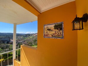 Un balcon donnant sur un paysage rural, une œuvre d’art en mosaïque et un luminaire fixé au mur.