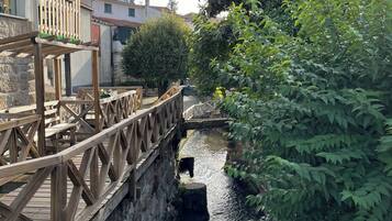 Un puente de madera cruza un estrecho canal de agua, rodeado de follaje y muros de piedra.