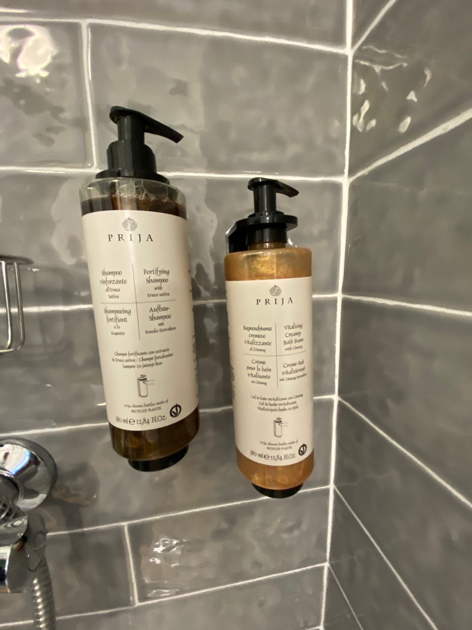 Two bottles of PRIJA shampoo and conditioner on a tiled wall.