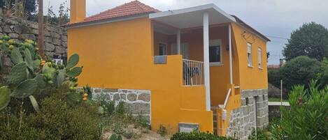 A yellow house with a stone foundation, a white porch, and a small balcony.