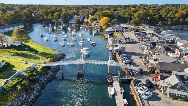 Ein Yachthafen mit vertäuten Booten, eine Fußgängerbrücke und Gebäude entlang des Ufers.