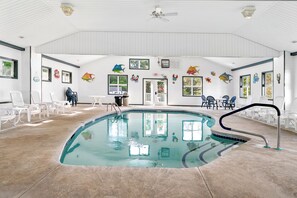 An indoor swimming pool with clear water, surrounded by white chairs and tables, and decorated with fish wall art.