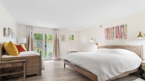 Ein Schlafzimmer mit Bett, Schreibtisch und Stuhl. Es gibt ein Fenster mit Vorhängen, eine Wandlampe und ein farbenfrohes Kunstwerk.