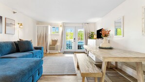 Ein Wohnzimmer mit einem blauen Sofa, einem Holzesstisch und Blick durch eine Glastür.