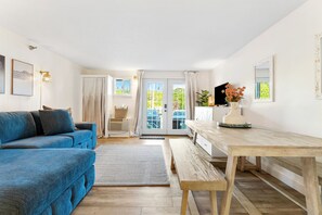 A living room with a blue sofa, a wooden dining table, and a view through a glass door.