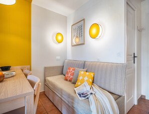 A cozy living area with a sofa, a dining table, and two wall-mounted lamps. - Family Suite With Garden Terrace (Mandelieu-La-Napoule)