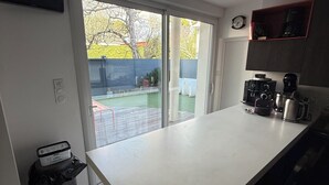 A kitchen with a white countertop, a trash bin, a coffee maker, and a clock on the wall.