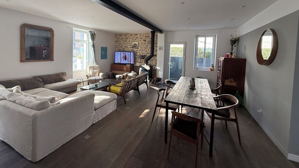 A modern living room with a sofa, TV, stone wall, and dining area.