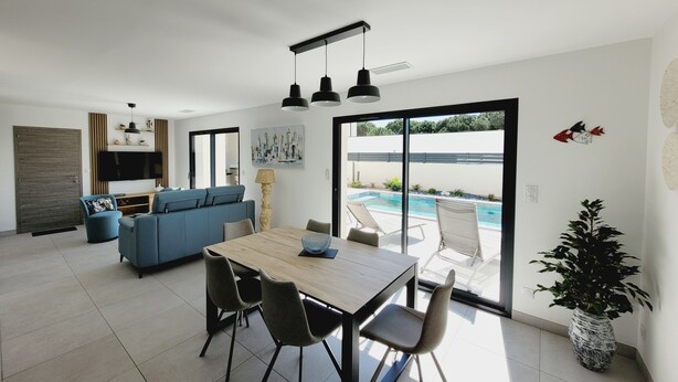 Ein modernes Wohnzimmer mit Essbereich, einer Couch, einem Fernseher und Blick auf einen Swimmingpool.