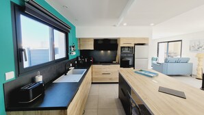 Eine moderne Küche mit großem Fenster, Holzschränken und einer Essecke mit Tisch und Stühlen.