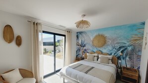 A bedroom with a bed, a chair, a mural, and a view through a sliding door. - Villa Elma, heated pool & close to the beach (Sérignan)
