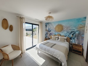 Ein Schlafzimmer mit Bett, Stuhl, Wandgemälde und Blick durch eine Schiebetür.
