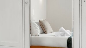 Een witte kast met spiegel, een bed met witte lakens en een houten hoofdbord, en een klein rood kunstwerk aan de muur.