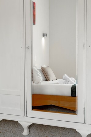 A white wardrobe with a mirror, a bed with white linens and a wooden headboard, and a small red artwork on the wall. - Charming 2BR Apartment with Balcony in Valletta Old Town (Valletta)