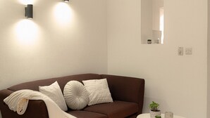 Een moderne woonkamer met een bruine bank, een ronde witte salontafel en twee wandlampen.