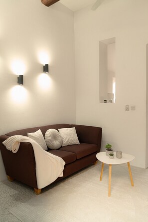 A modern living room with a brown sofa, a round white coffee table, and two wall-mounted lights. - Charming 2BR Apartment with Balcony in Valletta Old Town (Valletta)