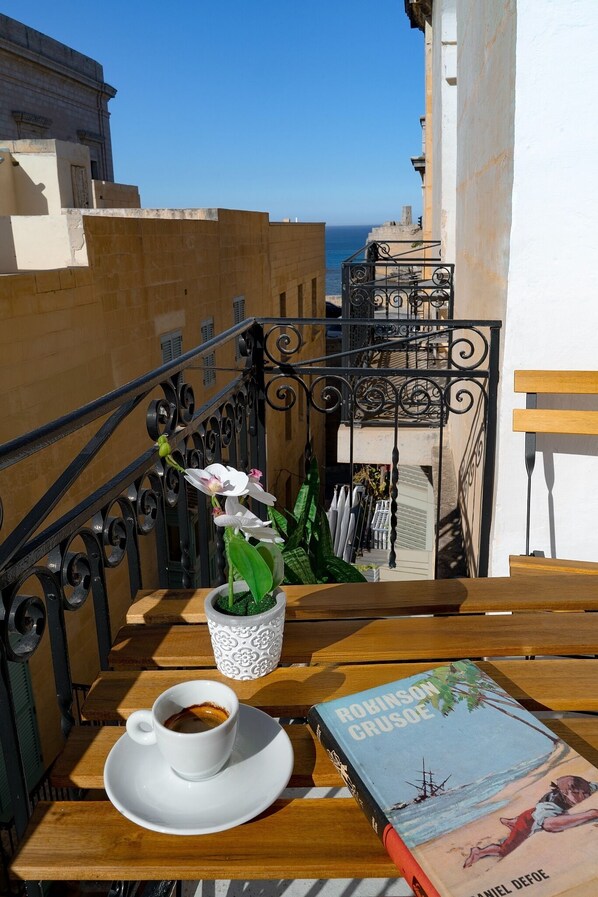 A balcony with a table, a book, a cup of coffee, and a potted plant. - Charming 2BR Apartment with Balcony in Valletta Old Town (Valletta)