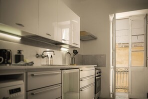A kitchen with white cabinets, a stainless steel range hood, a built-in oven, and a small refrigerator. - Charming 2BR Apartment with Balcony in Valletta Old Town (Valletta)