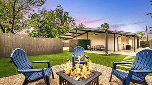 Ein Garten mit Feuerstelle, zwei Adirondack-Stühlen und einer überdachten Terrasse.