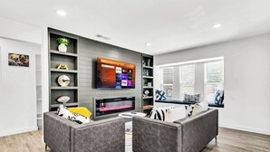 Ein modernes Wohnzimmer mit grauem Sofa, einem flachbildfernseher an einer grauen Wand und einem Kamin darunter.