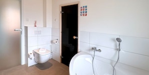 Een badkamer met toilet, douche en een deur naar een andere kamer.