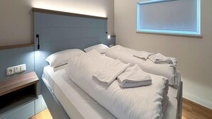 A double bed with white linens and a headboard, a bedside table, and a wall-mounted light fixture. - Ferienhaus mit Whirlpool und Sauna in Bad Bevensen (Bad Bevensen)