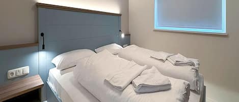 A double bed with white linens and a headboard, a bedside table, and a wall-mounted light fixture.