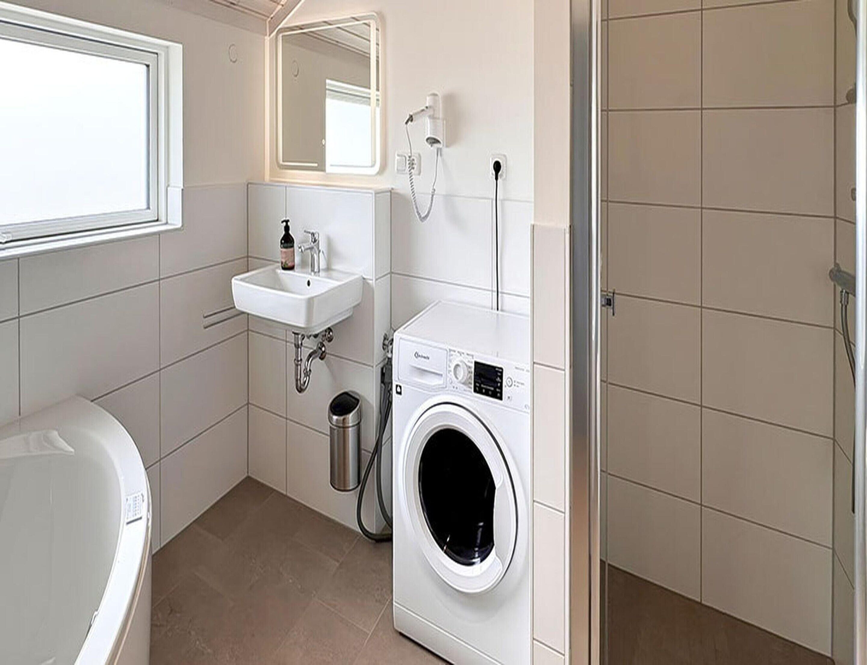 A compact bathroom with a white sink, a mirror, a washing machine, and a bathtub.