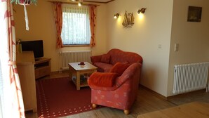 A cozy living room with a sofa, a small table, a TV, and a window with curtains. - Vacation home Mundt Between the Bodden and the Baltic Sea, at the very top in the north of Rügen (Altenkirchen OT Drewoldke)