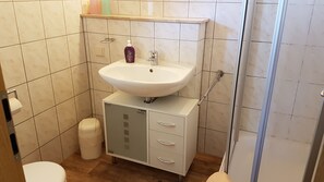 A bathroom with a white sink, a toilet, a trash bin, and a cabinet with drawers. - Vacation home Mundt Between the Bodden and the Baltic Sea, at the very top in the north of Rügen (Altenkirchen OT Drewoldke)