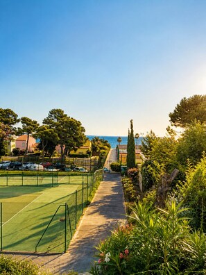 A tennis court with a pathway leading to a beach, surrounded by greenery and residential buildings. - The love nest (Mèze)
