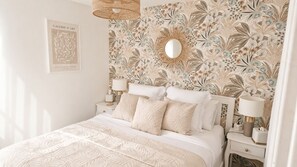 A bedroom with a floral wallpaper, a bed with white bedding, two bedside tables with lamps, and a framed artwork on the wall. - The love nest (Mèze)