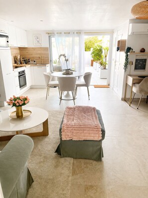 A modern kitchen with white cabinets, a dining area with a round table and chairs, and a cozy seating area with a bench. - The love nest (Mèze)