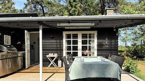 Eine Holzhütte mit Terrasse, Grill und Esstisch für vier Personen.