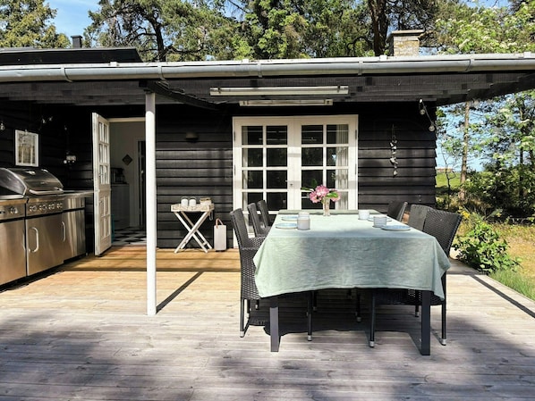 Eine Holzhütte mit Terrasse, Grill und Esstisch für vier Personen.