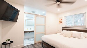A bedroom with a bed, a ceiling fan, a window with blinds, a wall-mounted TV, and a bathroom with a mirror and sink. - FIFA World Cup 2026 · 4BR Saltwater Pool · 15 Min Hard Rock (Hollywood)
