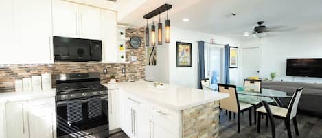 A modern kitchen with white cabinets, a built-in stove, and a dining area with a glass table and chairs.