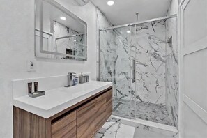 A modern bathroom with a marble shower, a large mirror, and a wooden vanity. - FIFA World Cup 2026 · 4BR Saltwater Pool · 15 Min Hard Rock (Hollywood)
